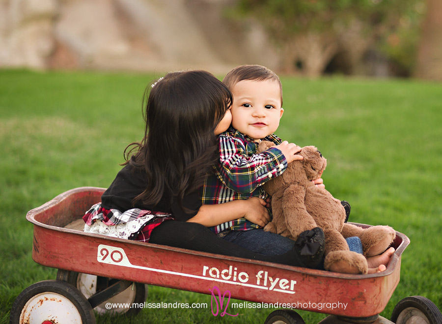 Sister kissing baby brother in red wagon at the park