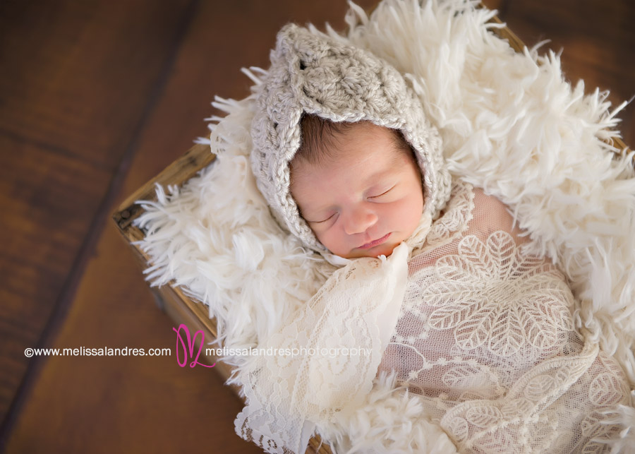 Newborn baby girl in box with white fun and handmade knit and lace bonnet
