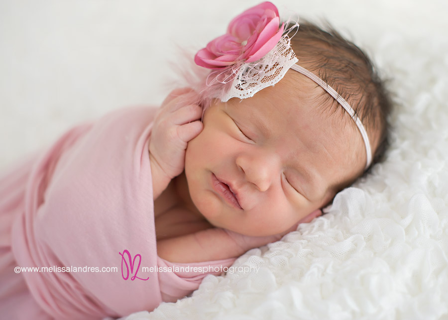 beautiful newborn baby girl wrapped in pink with matching headband on white lace blanket
