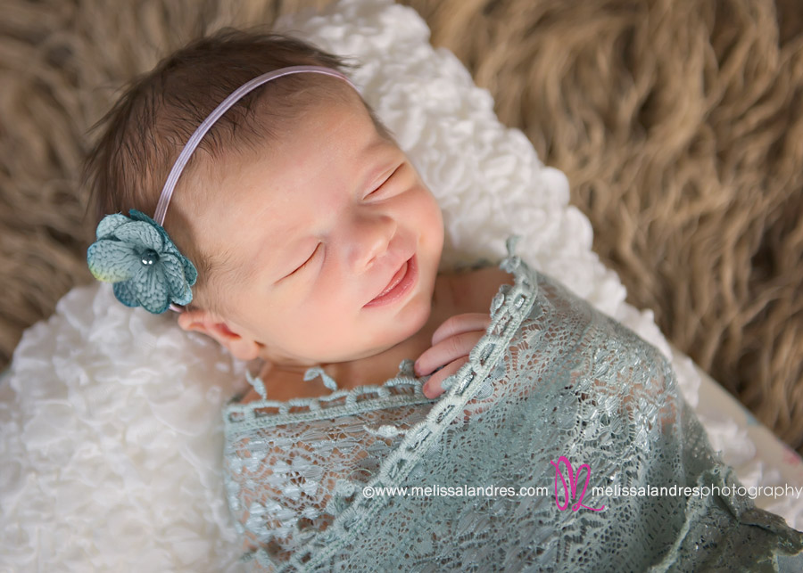 smiling newborn baby girl with light blue headband and lace wrap