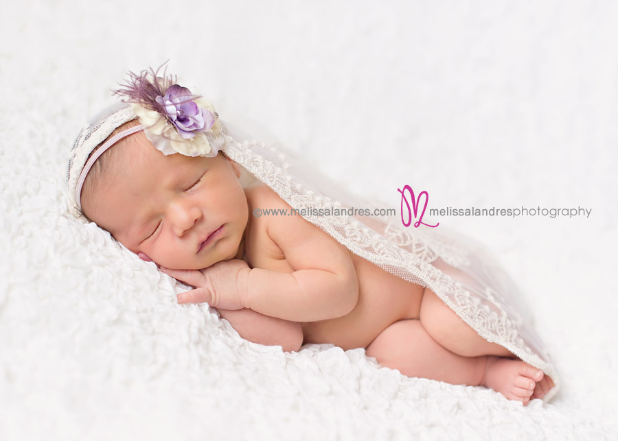 precious newborn baby girl on white lace blanket with delicate flower headband