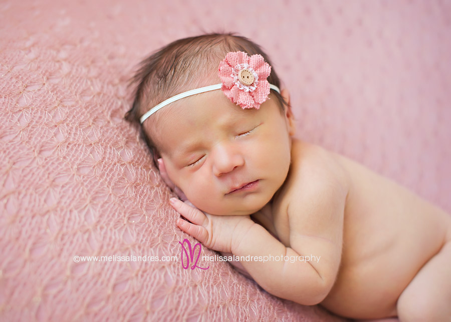 close up of newborn baby girl on beautiful pink knit blanket with matching handmade flower headband