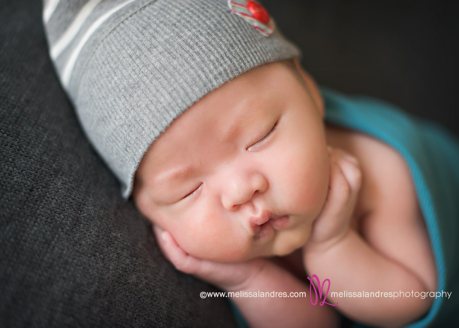 newborn baby boy wearing grey sleepy time cap; hand under chin