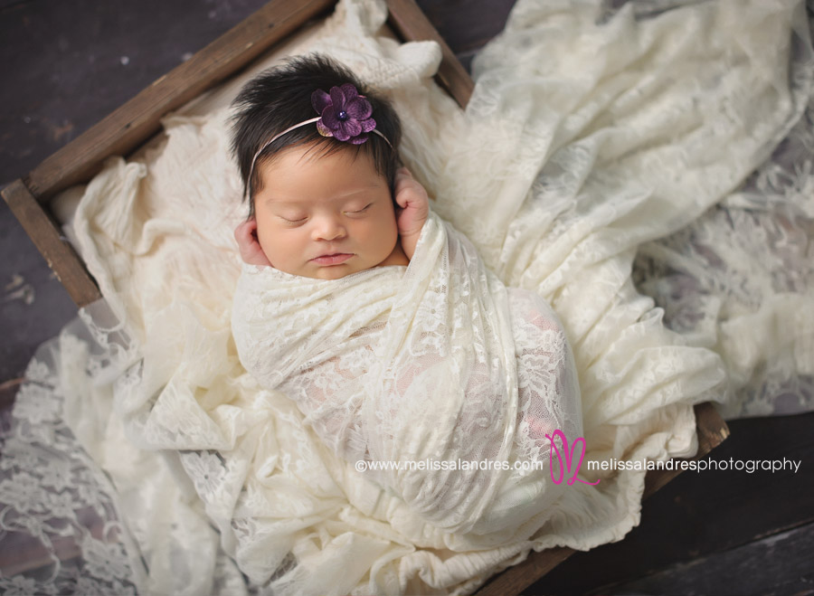 newborn baby wrapped in soft lace in wooden box with purple flower headband