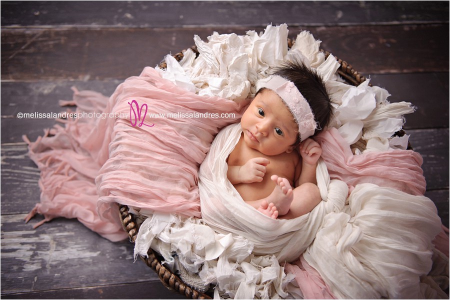 newborn baby girl awake poses, wrapped in pink and white layers in basket prop on aged wood floor