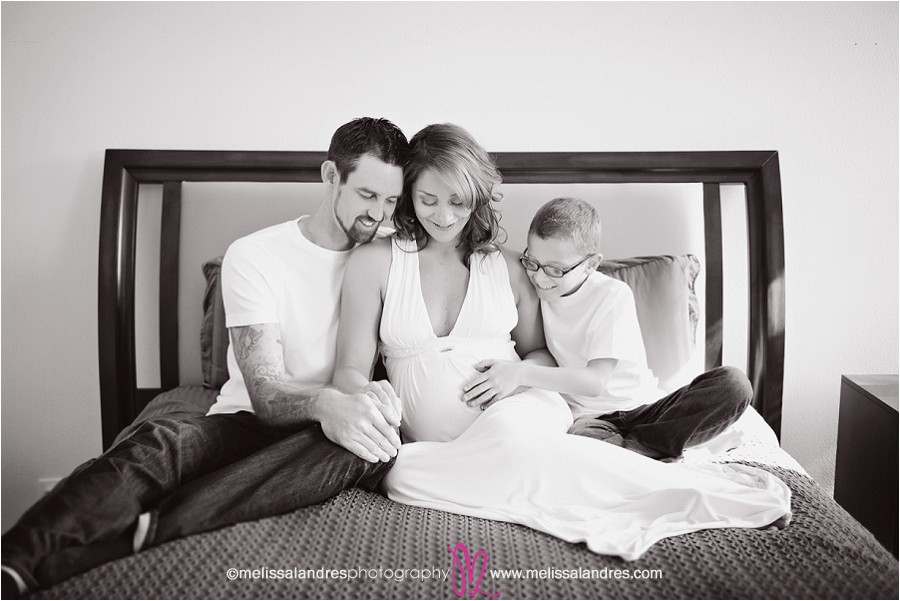 family looking down at mothers pregnant belly, natural relaxed maternity photos in home on the bed